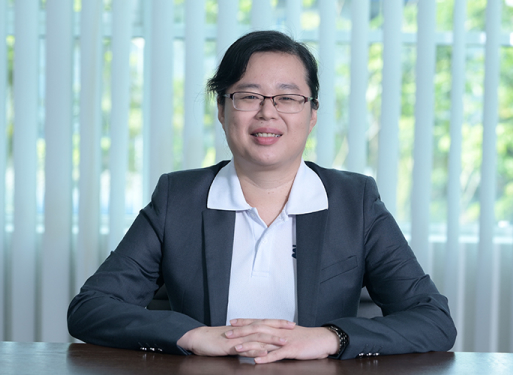 Frau Wong Meng Fong mit dunklem Anzug und weißem Hemd vor vertikalen, hellen Lamellen sitzend.