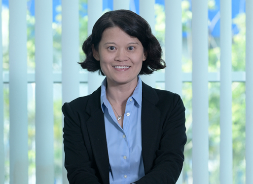 Person mit dunklem Anzug und weißem Hemd vor vertikalen, hellen Lamellen sitzend.