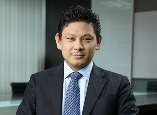 Porträt eines lächelnden Geschäftsmannes im Anzug vor einem modernen Bürohintergrund.