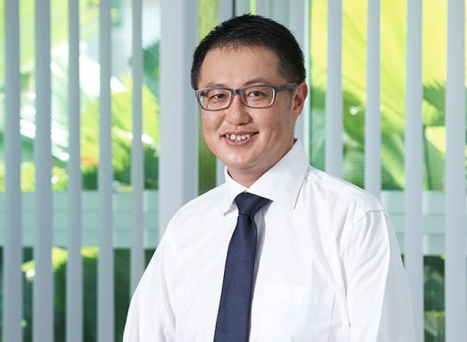 Herr Leong Moon Seng in weißem Hemd mit Krawatte vor vertikalen Jalousien