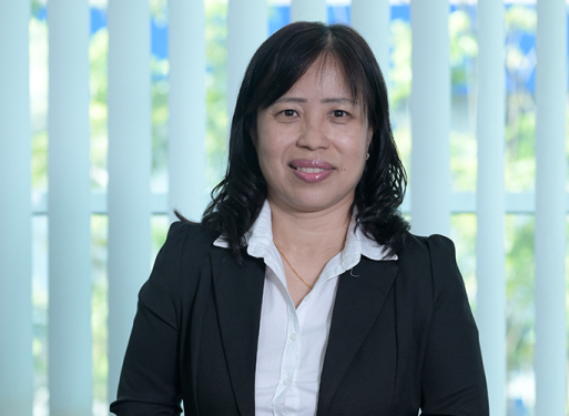 Frau Lock Wai Kuen mit dunklem Anzug und weißem Hemd vor vertikalen, hellen Lamellen sitzend.