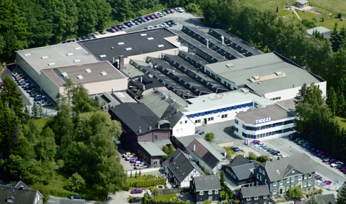 Luftaufnahme eines großen Industriegebäudes mit mehreren Parkplätzen und umgebenden Bäumen