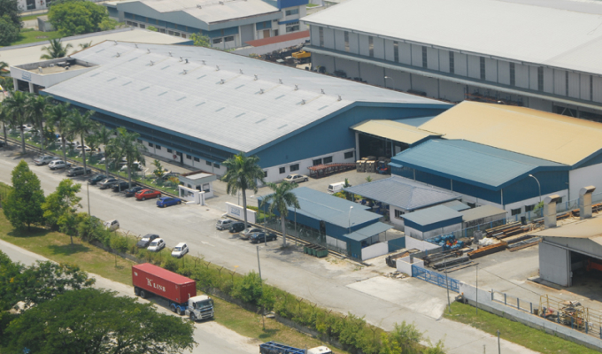 Luftaufnahme eines Industriegebiets mit mehreren großen Lagerhallen, LKWs und parkenden Autos entlang einer Straße.