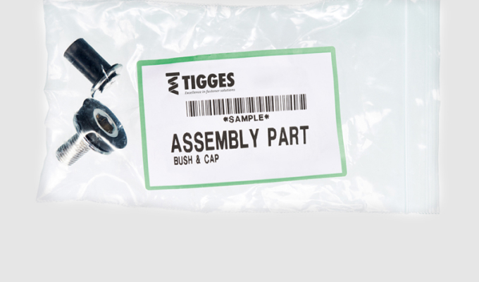 Plastiktüte mit Schraube und Kunststoffteil, darauf ein Etikett mit dem Text 'TIGGES ASSEMBLY PART BUSH & CAP'.