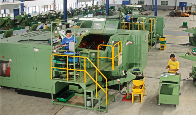 Große grüne Industriemaschine in einer Werkshalle, zwei Personen bedienen sie, eine schiebt einen Wagen mit Werkzeugen.