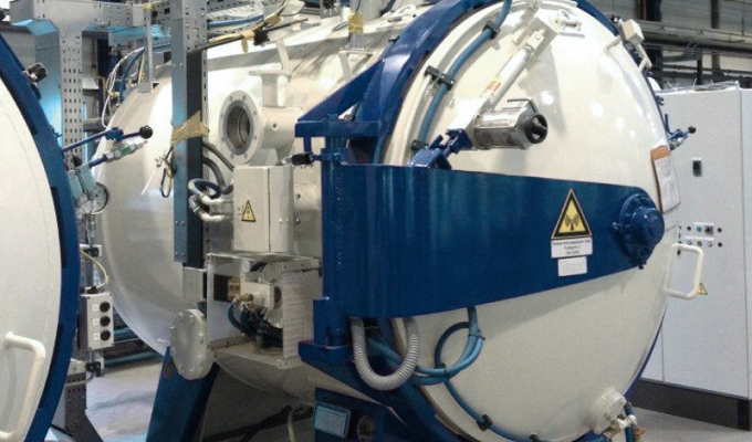 Große industrielle Maschine mit rundem, weißem Druckbehälter und blauem Schutzgehäuse in einer Fabrikumgebung.