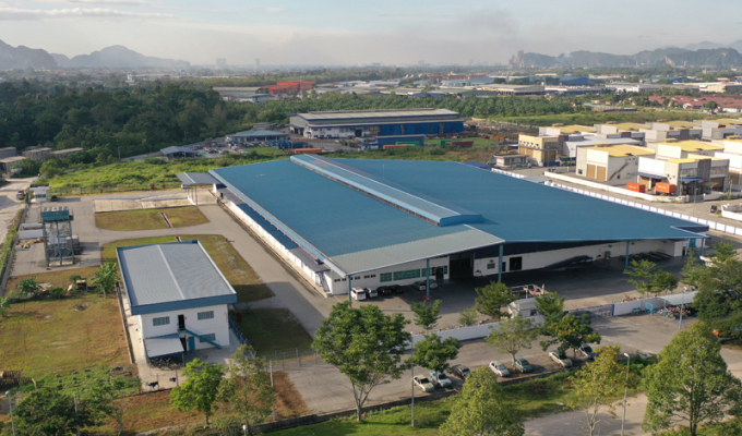 Luftaufnahme eines Industriegebiets mit mehreren großen Lagerhallen und umgebenden Straßen, Bäumen und parkenden Autos.