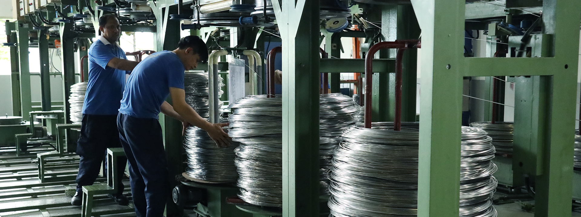 Mitarbeiter überwachen den Drahtziehprozess in der industriellen Fertigung, große aufgewickelte Metalldrähte an Maschinen.
