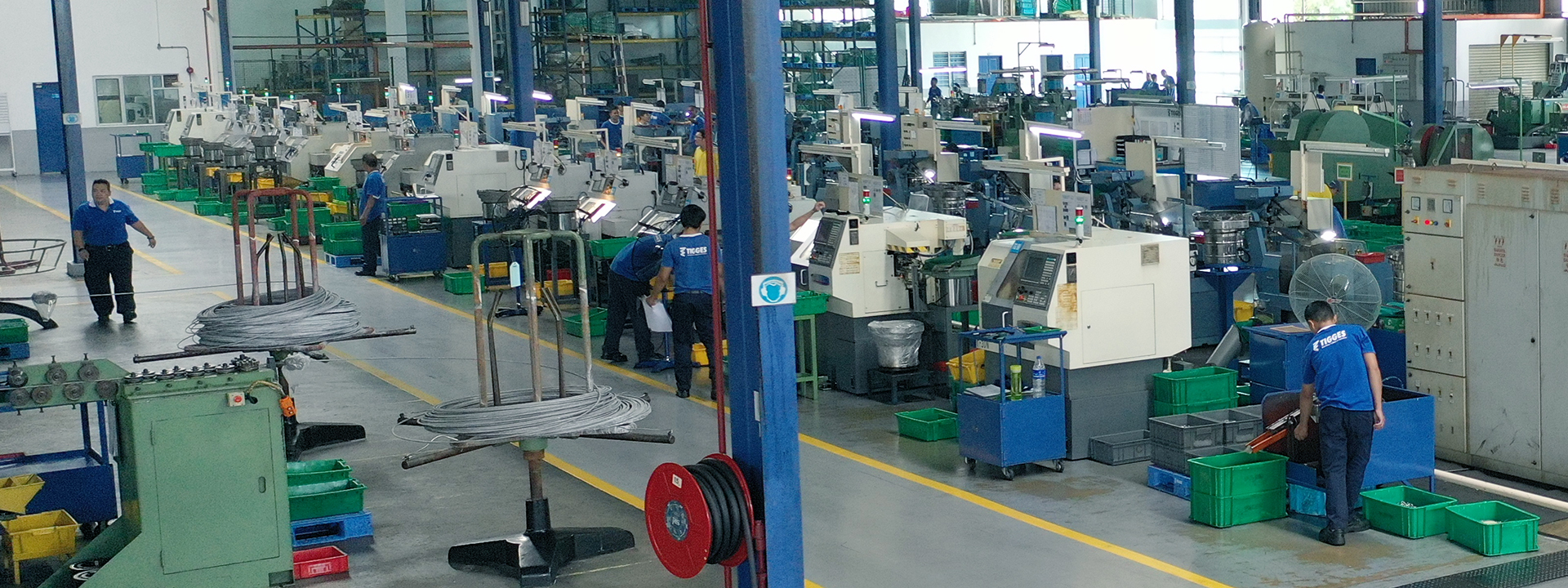 Produktionshalle mit CNC-Maschinen und Mitarbeitenden bei der Nachbearbeitung von Verbindungselementen