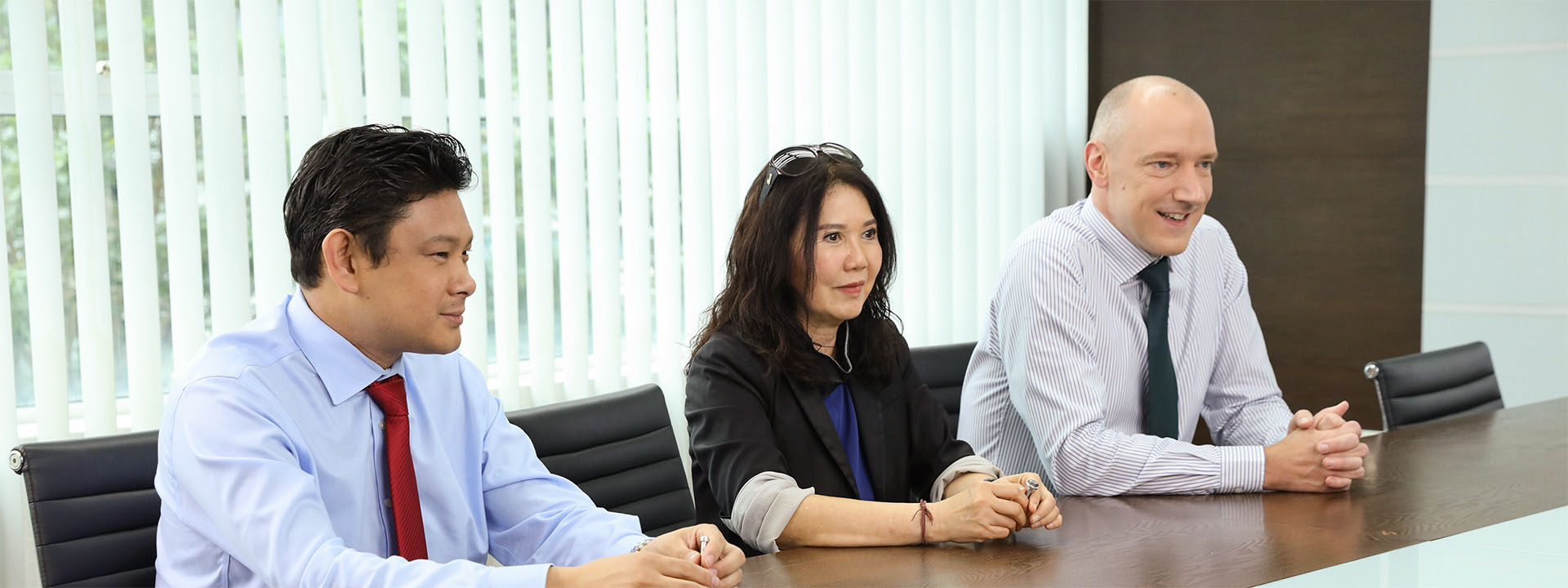 Drei Führungskräfte sitzen gemeinsam an einem Konferenztisch und besprechen strategische Themen in einem modernen Besprechungsraum.