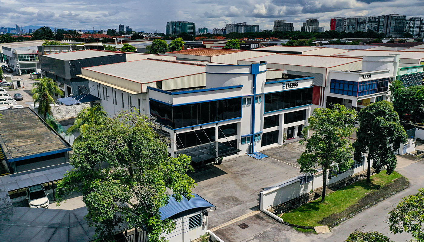 Luftaufnahme des TIGGES-Unternehmensstandorts mit Büro- und Produktionsgebäuden in einem Industriegebiet, umgeben von Grünflächen und städtischer Bebauung.