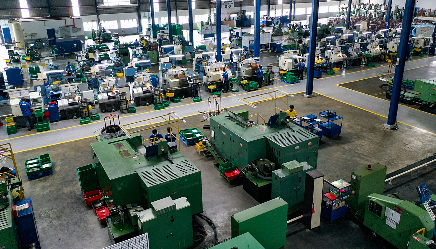 Blick in eine große industrielle Fertigungshalle mit zahlreichen Maschinen, Materialstationen und Mitarbeitenden im Produktionsbetrieb.