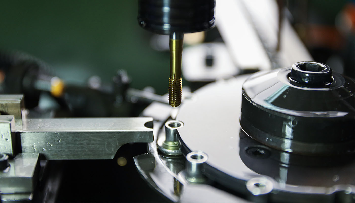 Nahaufnahme eines Gewindeschneidwerkzeugs bei der präzisen Bearbeitung eines Metallbauteils auf einer industriellen Produktionsmaschine.