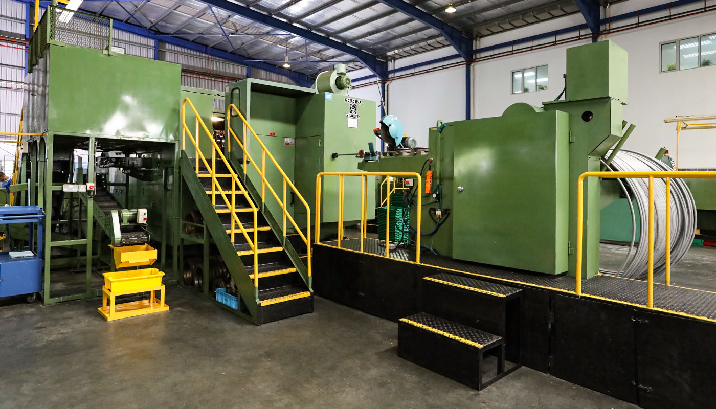 Große industrielle Produktionsanlage zur Metallverarbeitung in einer Fertigungshalle, mit Maschinen, Treppen und aufgewickeltem Draht.