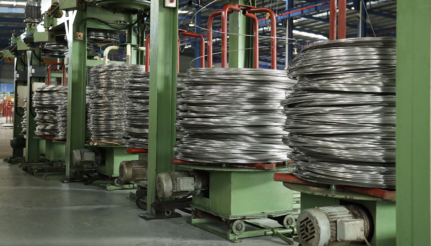 Aufgewickelter Metalldraht auf Spulen in einer industriellen Fertigungsanlage, Teil des Drahtzieh- und Produktionsprozesses.