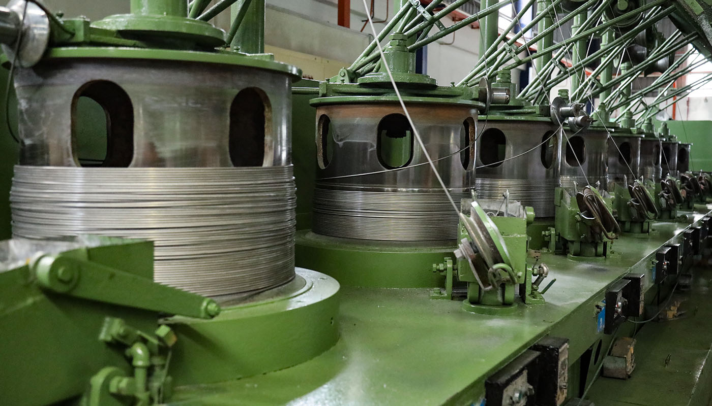 Drahtziehmaschine mit mehreren Spulen und Führungen in einer industriellen Produktionshalle, Teil der Metall- und Drahtverarbeitung.