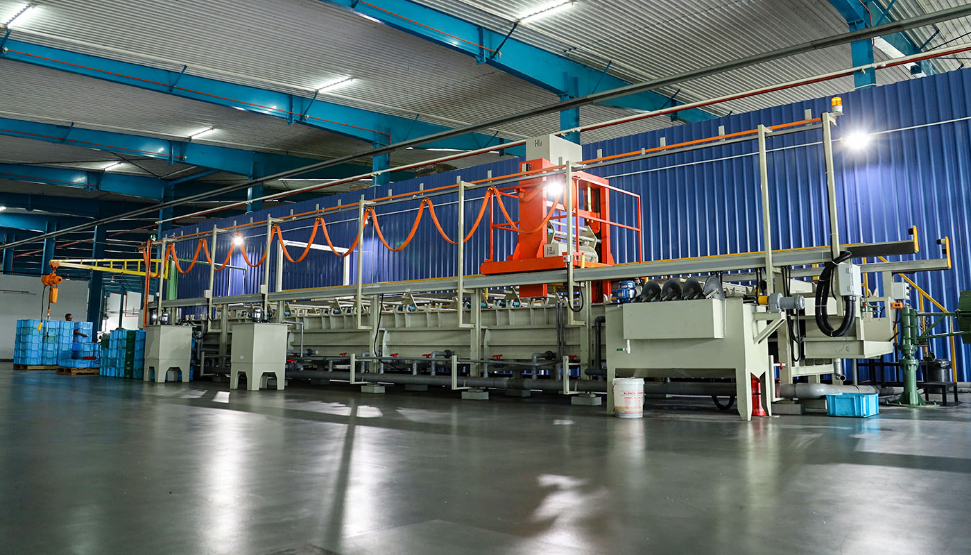 Moderne industrielle Produktionslinie in einer Werkhalle mit Anlagen zur Oberflächenbehandlung und Metallverarbeitung.