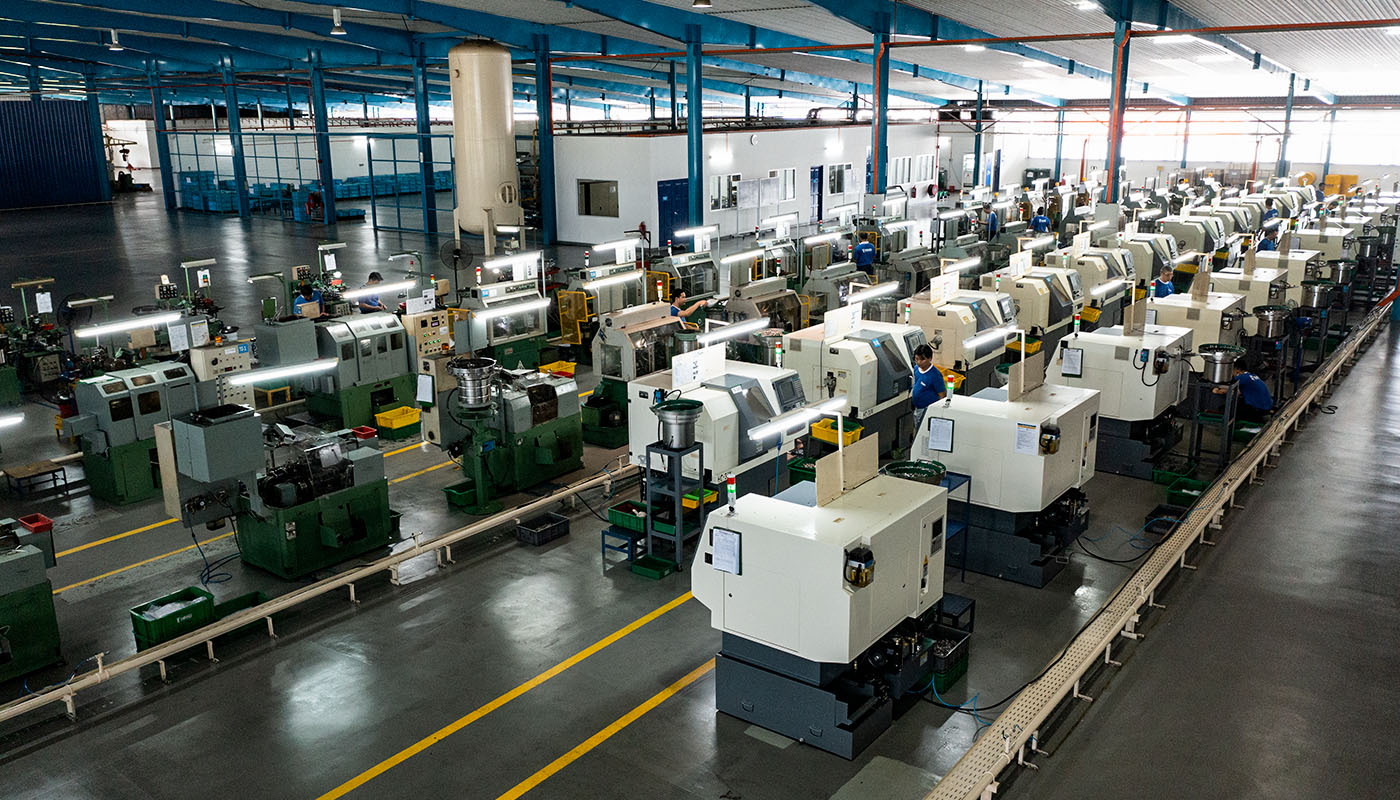 Große Fertigungshalle mit zahlreichen CNC-Maschinen und Produktionslinien zur Herstellung von Verbindungselementen, übersichtlich angeordnet in industrieller Umgebung.