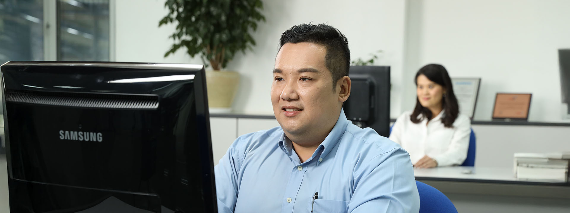 Mitarbeiter in einem modernen Büro am Computer, im Hintergrund arbeitet eine weitere Person